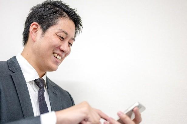 スマートフォンを見る笑顔の男性の画像